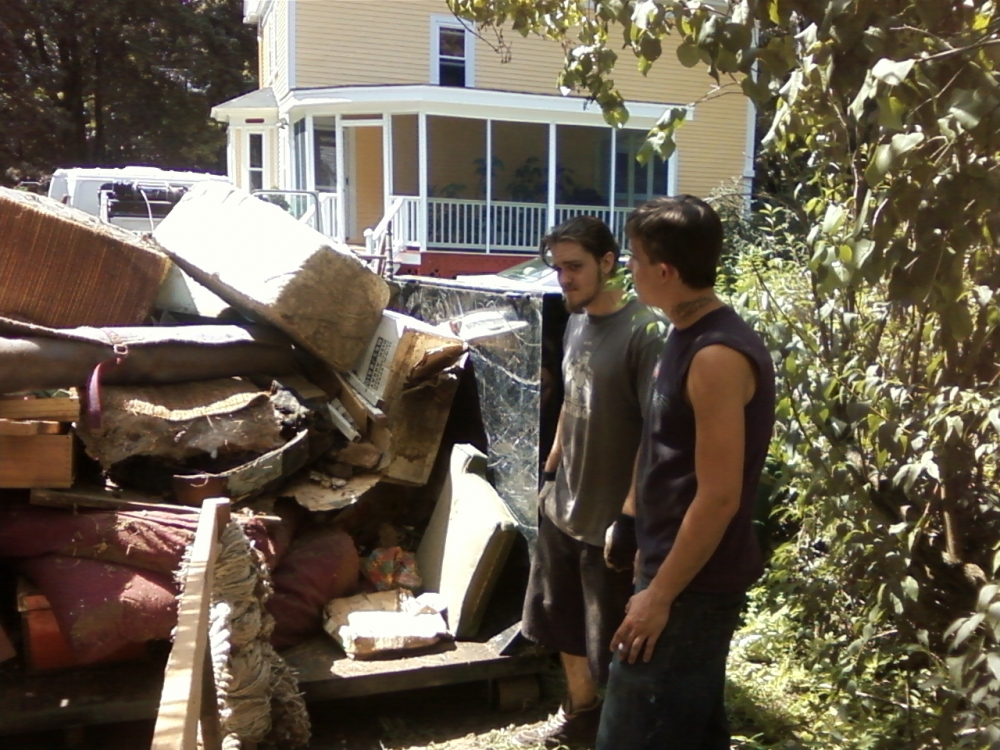 Two young men standing by a dumpster full of old furniture