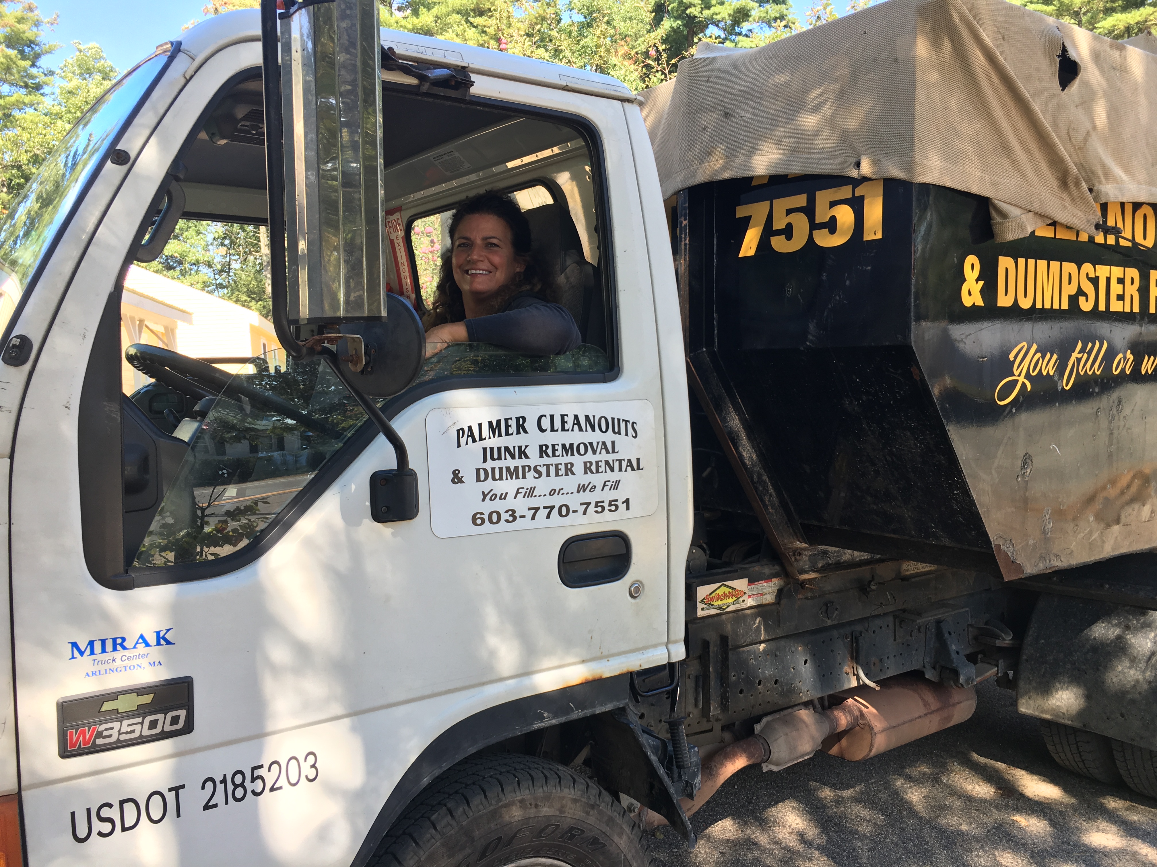 A smiling woman driving the Palmer Cleanouts & Disposal, LLC truck